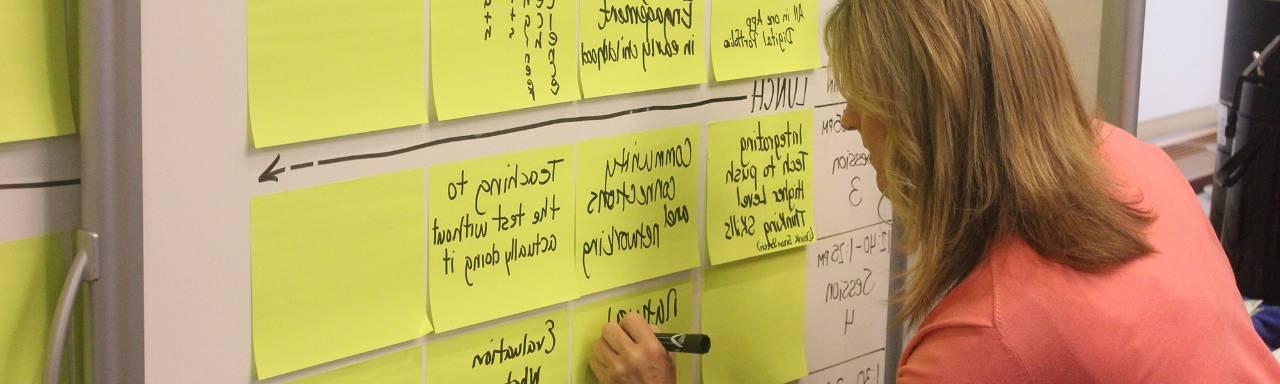 Woman writing notes on a whiteboard filled with sticky notes